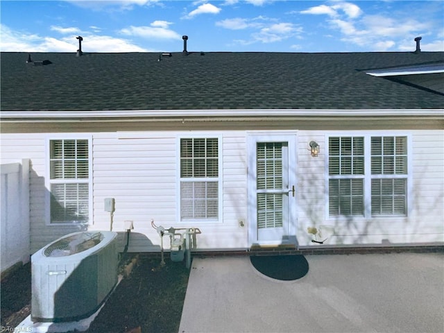 back of property with a patio area, a shingled roof, and central AC