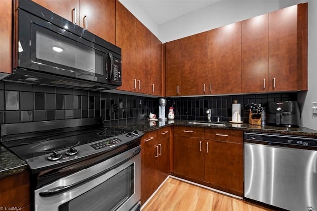 kitchen with light hardwood / wood-style floors, stainless steel appliances, sink, decorative backsplash, and dark stone countertops