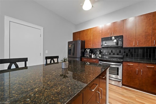 kitchen featuring light wood-type flooring, stainless steel appliances, dark stone counters, and tasteful backsplash