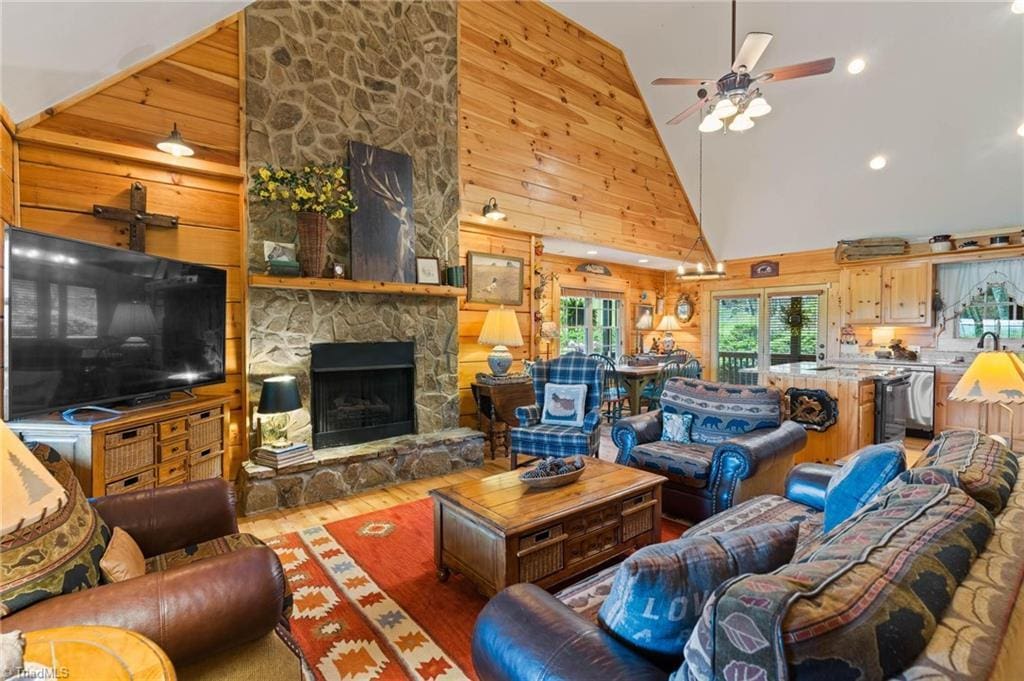 201 Cherokee Cir, Jefferson, NC 28640 - living area with high vaulted ceiling, wooden walls, a ceiling fan, a stone fireplace, and light wood finished floors