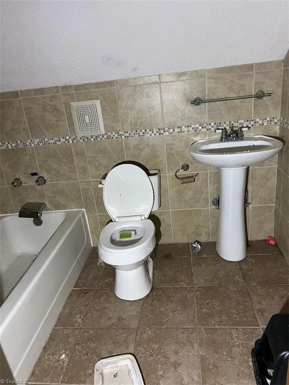 bathroom with toilet, a bathtub, and tile walls