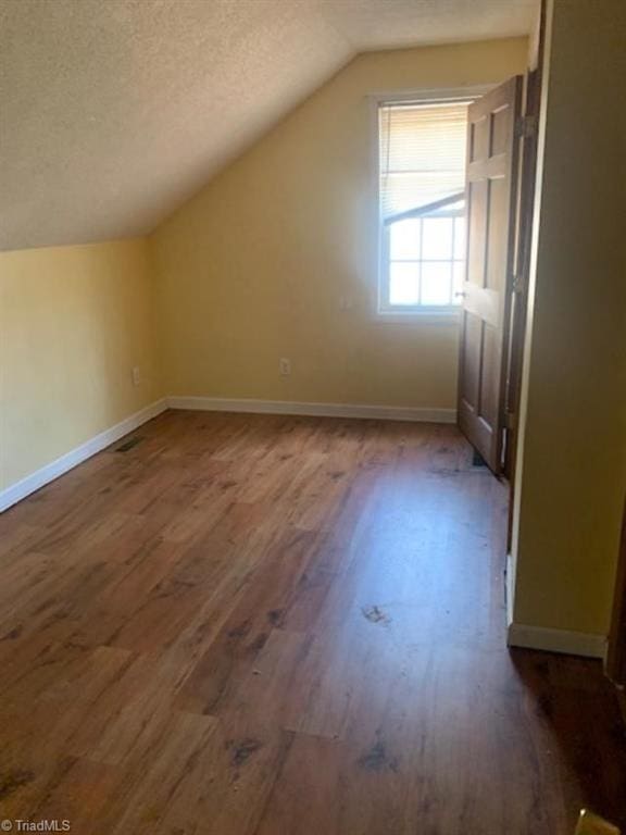 bonus room with a textured ceiling, vaulted ceiling, and dark wood-type flooring