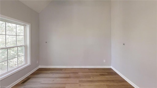 spare room with lofted ceiling, hardwood / wood-style flooring, and plenty of natural light