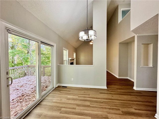 unfurnished dining area with baseboards, wood finished floors, a chandelier, and high vaulted ceiling