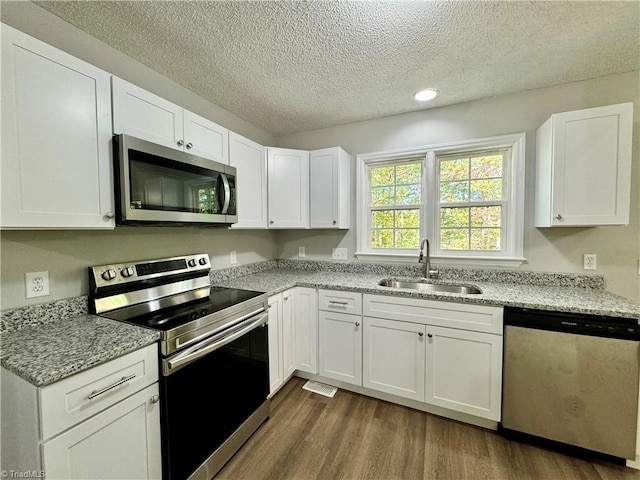 kitchen featuring dark wood-type flooring, sink, light stone countertops, white cabinetry, and appliances with stainless steel finishes