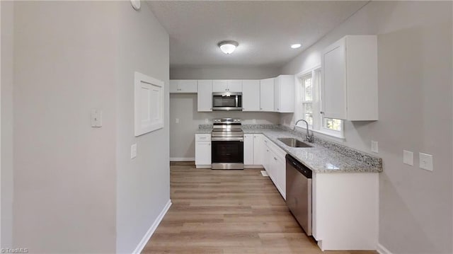 kitchen with stainless steel appliances, sink, light wood-type flooring, white cabinetry, and light stone counters