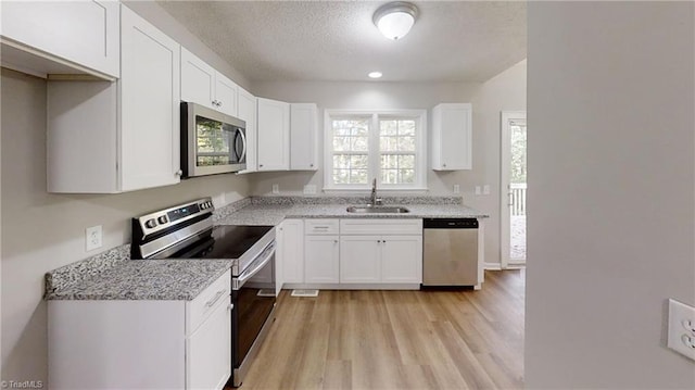 kitchen featuring stainless steel appliances, a sink, light wood-style floors, white cabinets, and light stone countertops