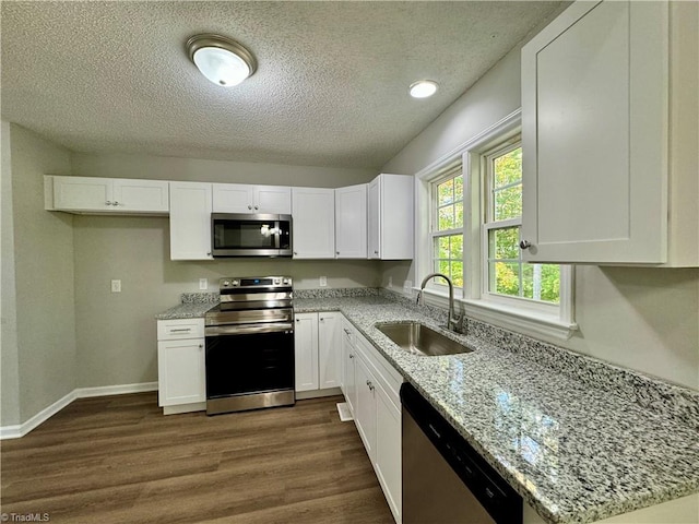 kitchen featuring appliances with stainless steel finishes, sink, white cabinets, dark wood-type flooring, and light stone counters