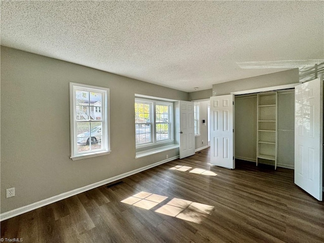 unfurnished bedroom with a textured ceiling, dark wood-style floors, baseboards, and a closet