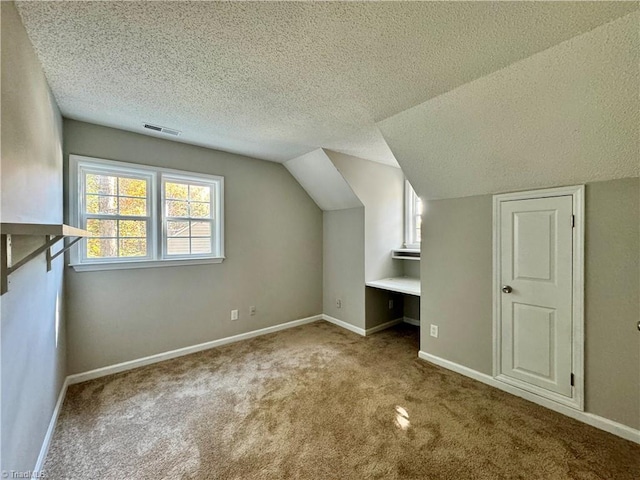 bonus room with built in desk, vaulted ceiling, a textured ceiling, and carpet floors