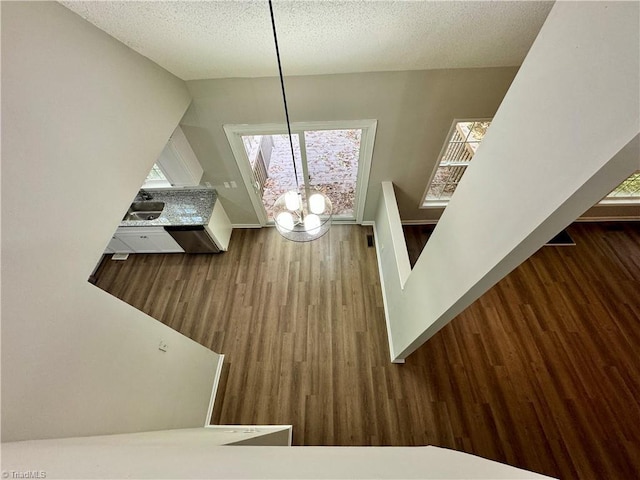 stairway with wood finished floors, healthy amount of natural light, a chandelier, and a textured ceiling