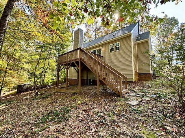 rear view of house featuring stairs, a wooden deck, a chimney, a shingled roof, and central AC unit