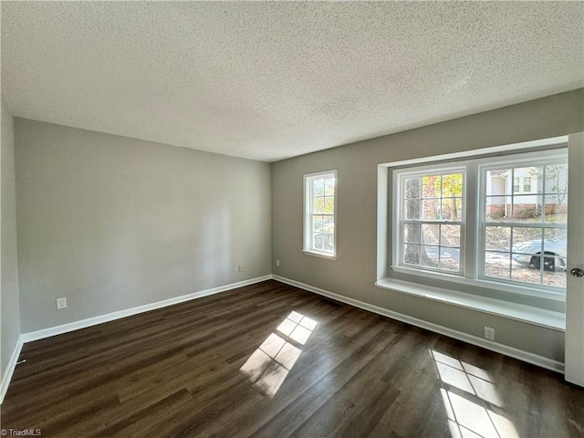 spare room featuring dark wood-type flooring, a textured ceiling, and baseboards