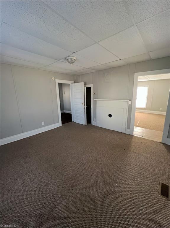 empty room with a paneled ceiling and dark colored carpet