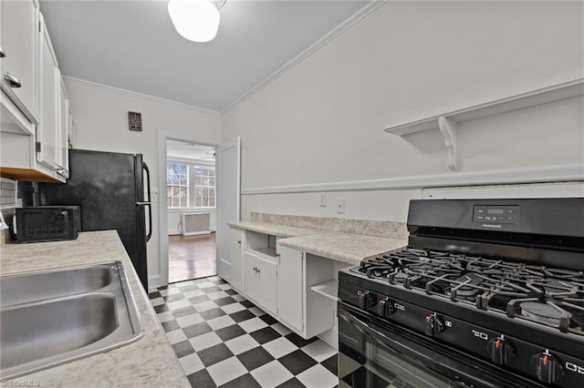 kitchen with dark floors, light countertops, black gas range oven, white cabinets, and a sink