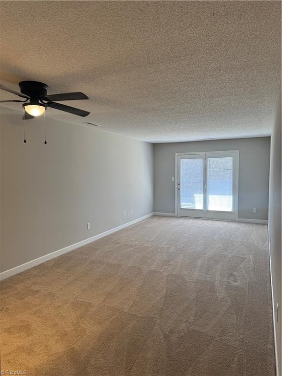 carpeted empty room with ceiling fan and a textured ceiling