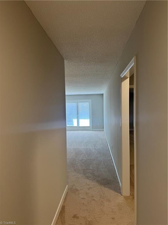 corridor with light carpet and a textured ceiling