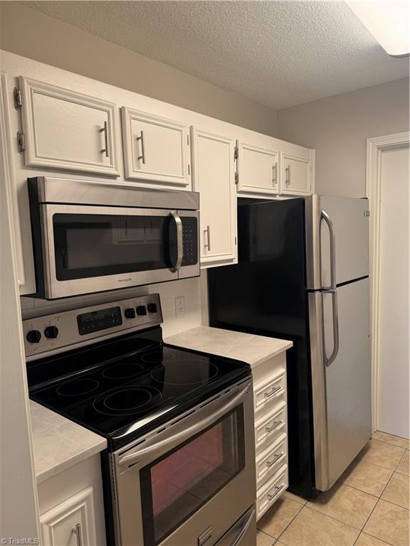 kitchen featuring stainless steel appliances, light tile patterned floors, a textured ceiling, and white cabinets