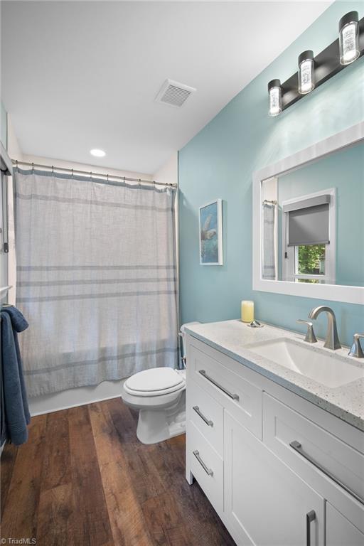 bathroom with toilet, shower / tub combo with curtain, visible vents, vanity, and wood finished floors