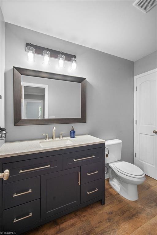 bathroom with toilet, vanity, visible vents, and wood finished floors