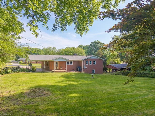 back of house with central air condition unit, an attached carport, and a lawn