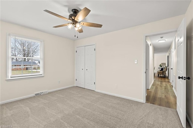 unfurnished bedroom featuring visible vents, light carpet, baseboards, and a closet