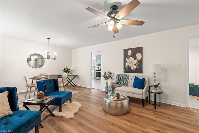 sitting room with ceiling fan with notable chandelier, baseboards, and wood finished floors