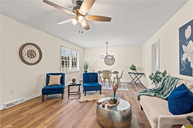 living area with visible vents, ceiling fan with notable chandelier, baseboards, and wood finished floors