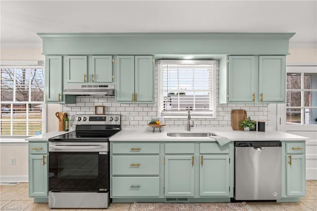 kitchen with green cabinets, under cabinet range hood, ornamental molding, stainless steel appliances, and a sink