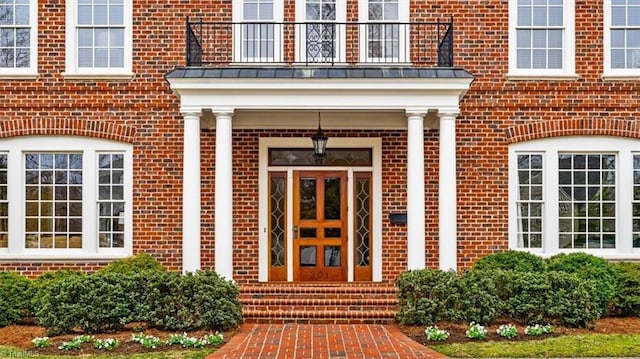 view of exterior entry with a standing seam roof, a balcony, brick siding, and metal roof