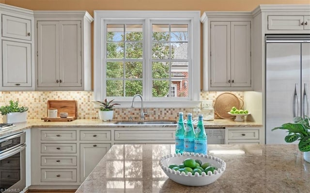 kitchen with decorative backsplash, light stone countertops, appliances with stainless steel finishes, and a sink