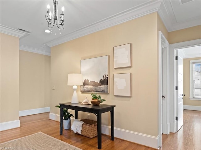 hallway with visible vents, wood finished floors, crown molding, baseboards, and a chandelier