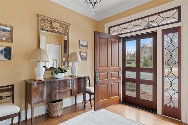 foyer entrance with an inviting chandelier, crown molding, wood finished floors, and baseboards