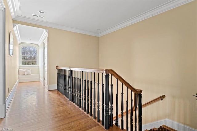 corridor with visible vents, baseboards, ornamental molding, an upstairs landing, and wood finished floors