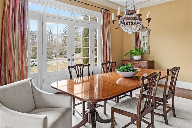 dining space featuring wood finished floors, baseboards, an inviting chandelier, ornamental molding, and french doors