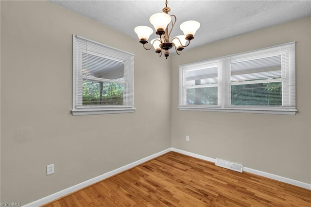 unfurnished room with a textured ceiling, hardwood / wood-style floors, and a chandelier