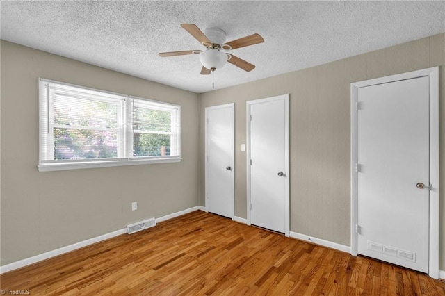 unfurnished bedroom with ceiling fan, multiple closets, a textured ceiling, and light hardwood / wood-style flooring