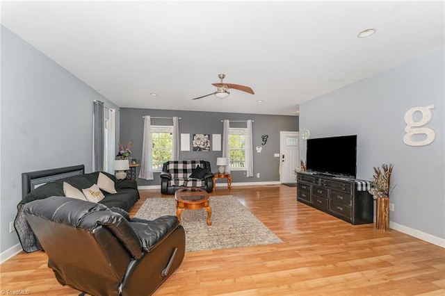 living room with baseboards, a ceiling fan, and light wood-type flooring