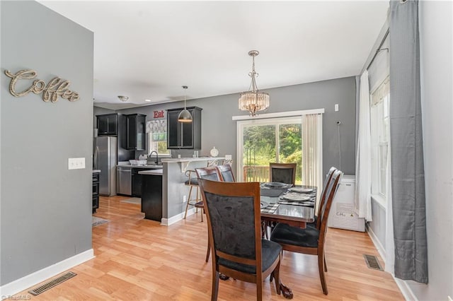 dining area featuring a chandelier, baseboards, visible vents, and light wood-style floors