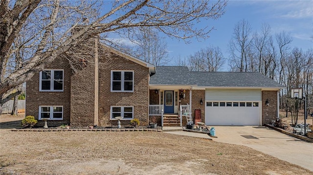 tri-level home featuring a garage, driveway, brick siding, and covered porch