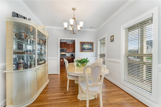 dining space with light wood-type flooring, crown molding, and an inviting chandelier