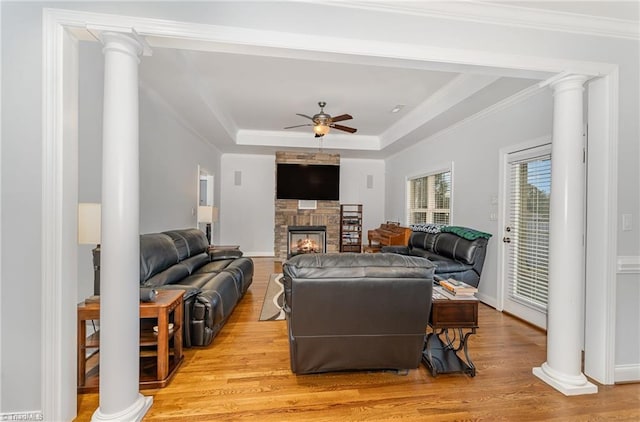 living room with ornamental molding, ceiling fan, a fireplace, a raised ceiling, and light wood-type flooring