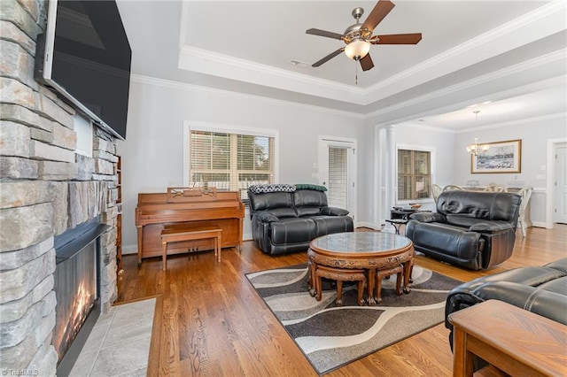 living room featuring a fireplace, a raised ceiling, light wood-type flooring, and crown molding