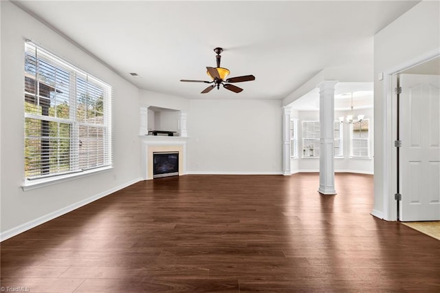 unfurnished living room with dark wood-type flooring, ceiling fan with notable chandelier, and decorative columns