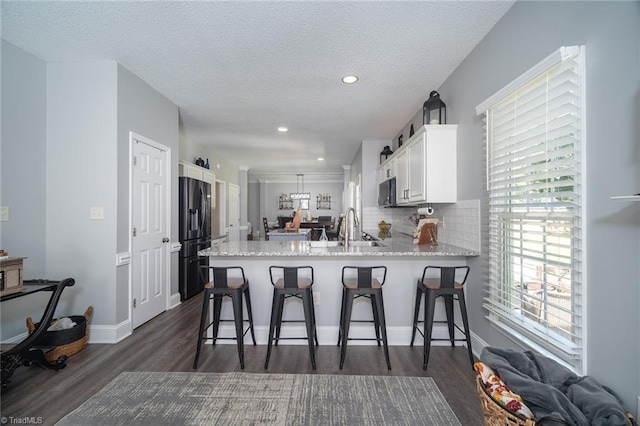 kitchen featuring black fridge with ice dispenser, sink, kitchen peninsula, white cabinetry, and a kitchen breakfast bar