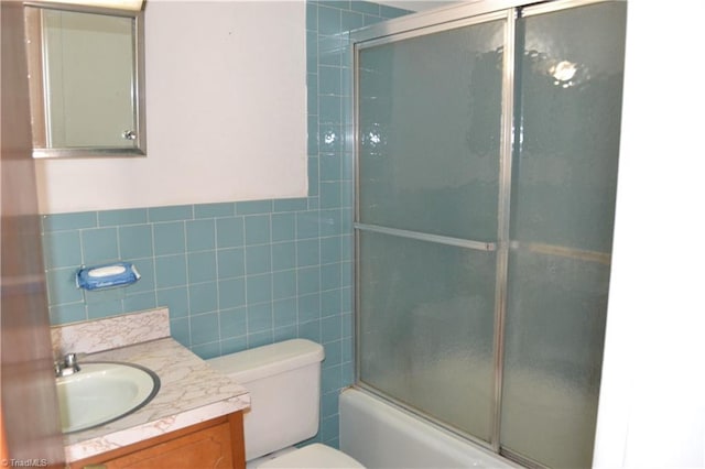 full bathroom featuring tile walls, bath / shower combo with glass door, toilet, and vanity