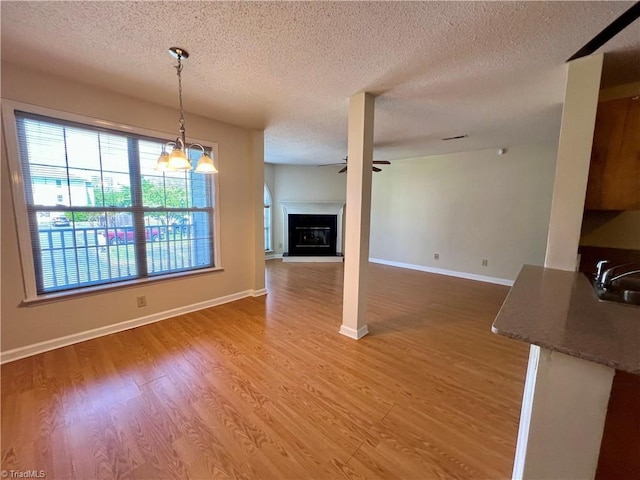 3638 Morris Farm Dr, Greensboro, NC 27409 - unfurnished living room featuring a textured ceiling, light wood-style floors, a ceiling fan, a fireplace with raised hearth, and baseboards