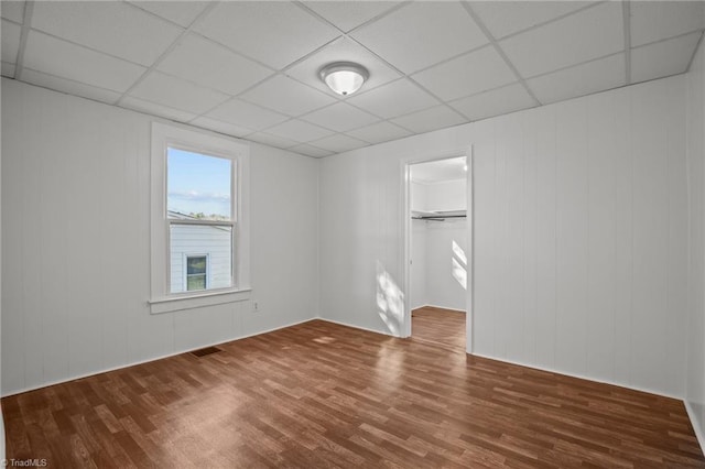 unfurnished bedroom featuring a spacious closet, a closet, a drop ceiling, and wood finished floors