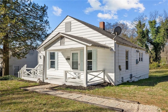 rear view of property featuring a yard, a porch, and a chimney