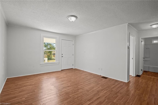 unfurnished room with a textured ceiling, ornamental molding, and wood finished floors